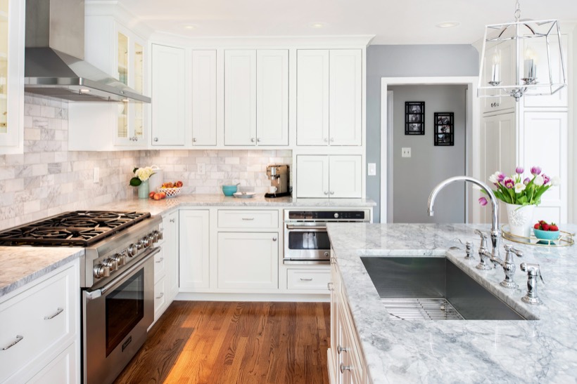 Bright, modern kitchen with Shiloh cabinetry, stainless steel appliances, marble countertops, a large island with a sink, wooden flooring, and a vase of tulips. Fruits and a coffee maker are on the counters