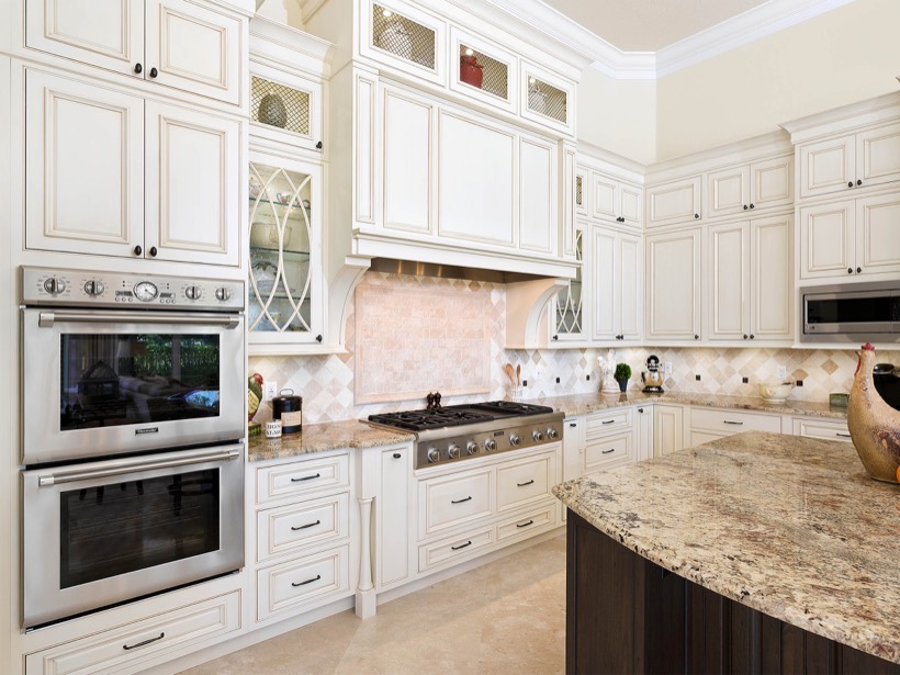 Elegant kitchen with cream-colored Shiloh cabinetry, stainless steel double oven, gas cooktop, beige tiled backsplash, and granite countertops. A large island with a dark wood base stands in the foreground of home