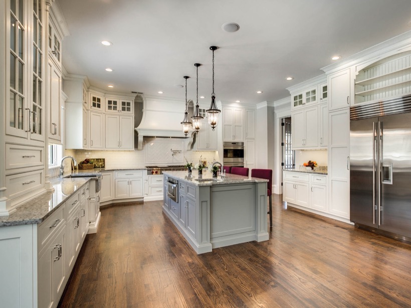 Shiloh cabinetry example, spacious, modern kitchen with sleek white kitchen cabinets, stainless steel appliances, a large central island with gray base and built-in oven, pendant lights, and hardwood floors