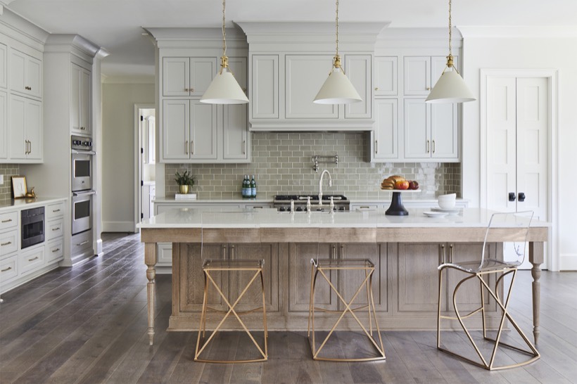 Shiloh cabinetry example, a modern kitchen with light gray kitchen cabinets, a large island featuring a marble countertop, three stylish barstools, pendant lights, stainless steel appliances, hardwood floors, and a sophisticated neutral color palette