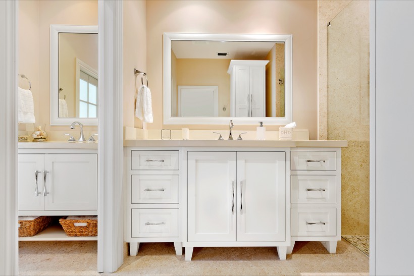A modern bathroom with a large vanity featuring sleek Shiloh cabinetry and drawers, a wide mirror above the sink, neatly folded towels, and a walk-in shower with a glass partition on the right