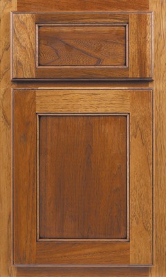 Shiloh Square Flat, A close-up of a wooden kitchen cabinet door and matching drawer above, featuring medium brown wood with visible grain patterns and decorative trim