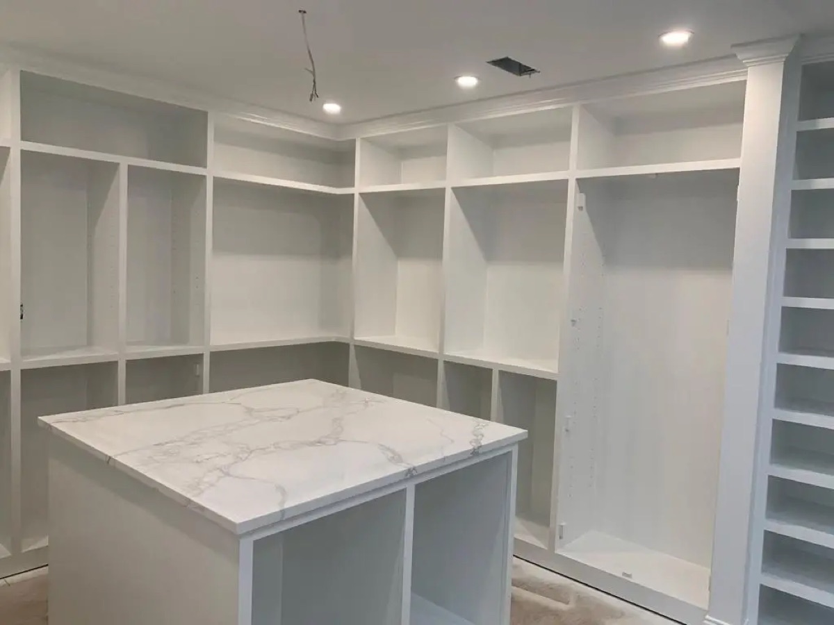 Custom white walk-in pantry by Bethesda Cabinets with open shelving and a marble-topped island.