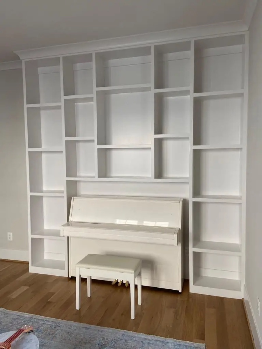 Custom white built-in shelving wall by Bethesda Cabinets framing an upright piano.