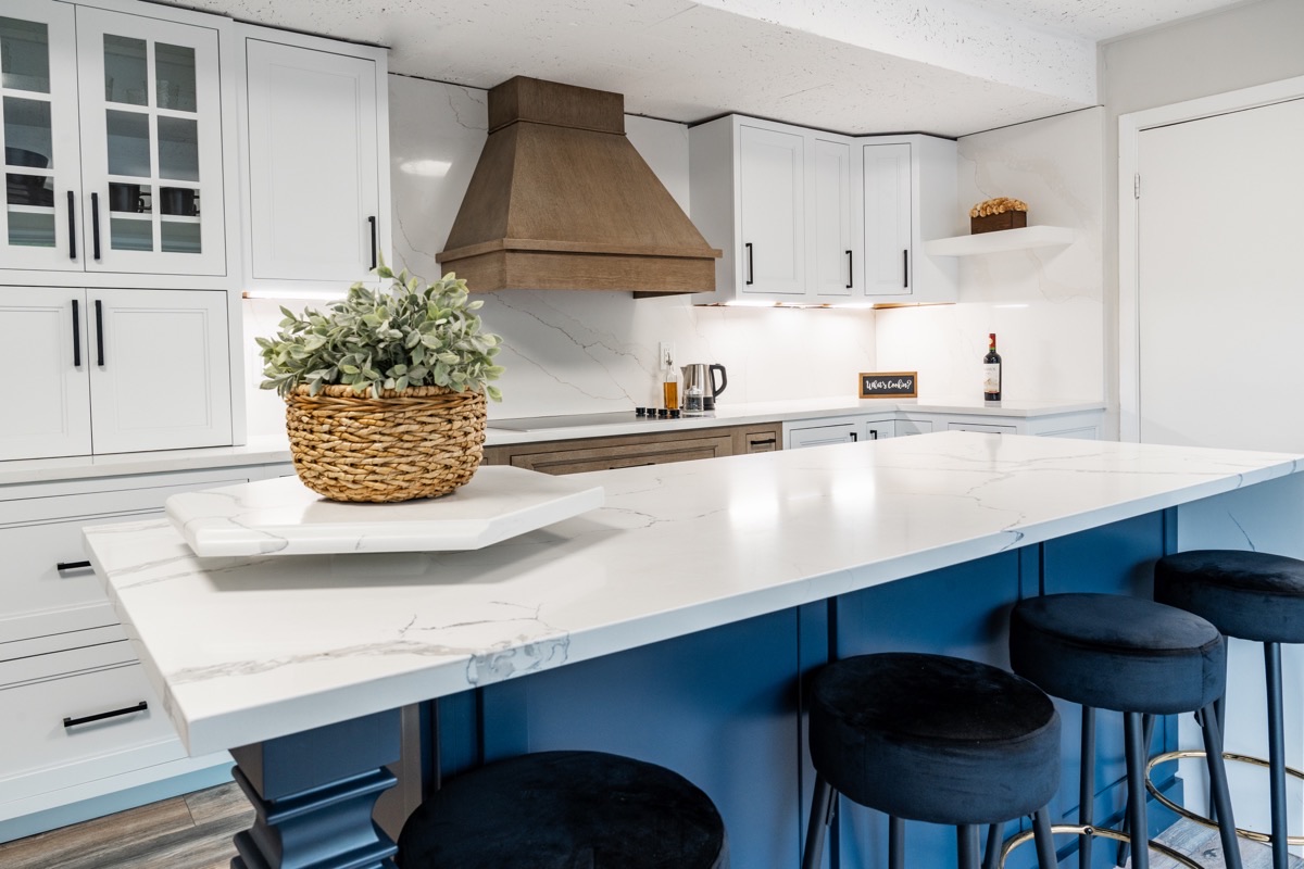 Full kitchen display at the Bethesda Cabinets showroom with white cabinets, a marble island, a blue base, and bar stools.