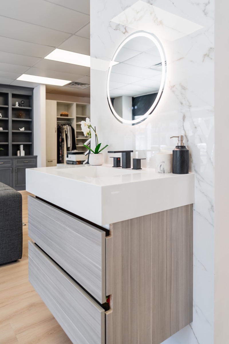 Bathroom vanity display at the Bethesda Cabinets showroom with a floating vanity, a large round backlit mirror, and a marble surround.