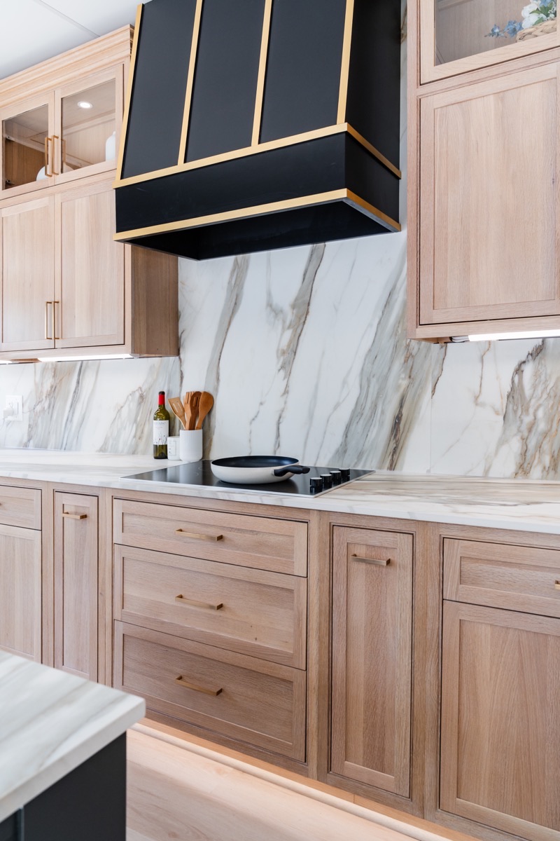 Kitchen display at the Bethesda Cabinets showroom with a white marble backsplash, a marble countertop, and warm wood cabinets.
