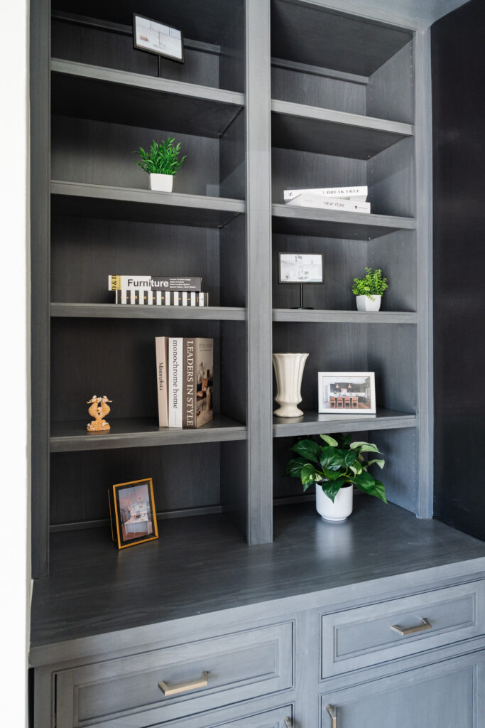 Dark gray built-in shelves with books, small potted plants, framed photographs, a white vase, and decorative objects neatly arranged on the shelves and countertop accentuate this MD homes style—perfect for pairing with matching kitchen cabinets.