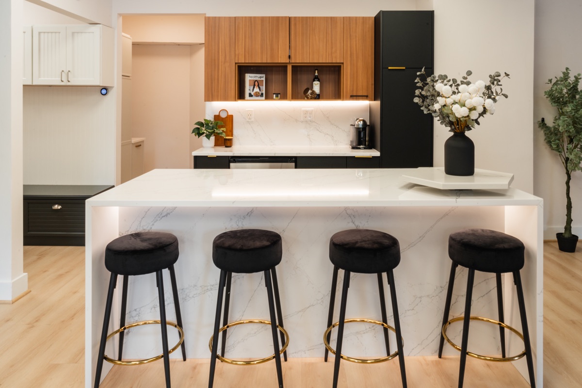 Kitchen display at the Bethesda Cabinets showroom with a marble-topped island, bar stools, and wood and black cabinets.