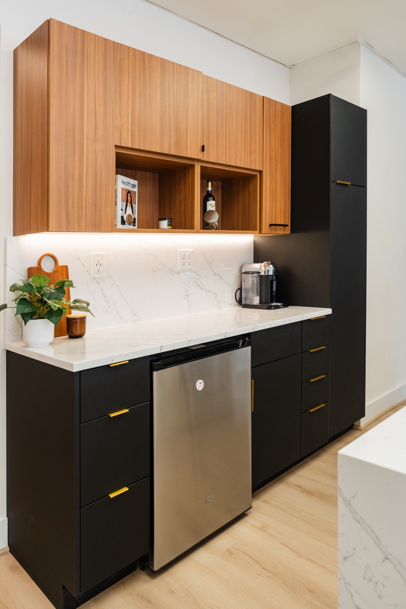 Kitchen display at the Bethesda Cabinets showroom with wood and black cabinets, a marble countertop, and built-in wine storage.