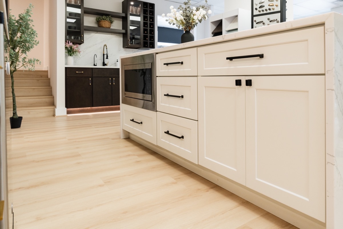 Kitchen display at the Bethesda Cabinets showroom with full-overlay white cabinets, black hardware, a built-in microwave, and a marble waterfall island.