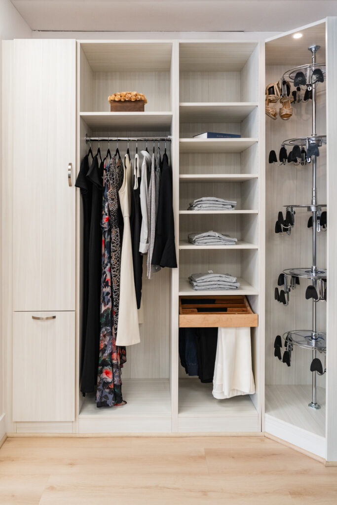A modern wardrobe with hanging dresses, jackets, and shirts, several open shelves with folded clothes, a pull-out drawer, and a corner rack for shoes. Crafted in light wood by Bethesda Cabinets, it boasts a clean, organized look perfect for Maryland homes.