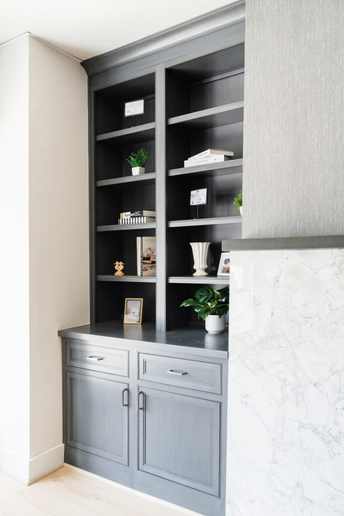 Built-in gray shelves by Bethesda Cabinets in DC and MD, styled with minimal decor—small potted plants, framed photos, a white vase, books—and a marble countertop partially visible on the right.