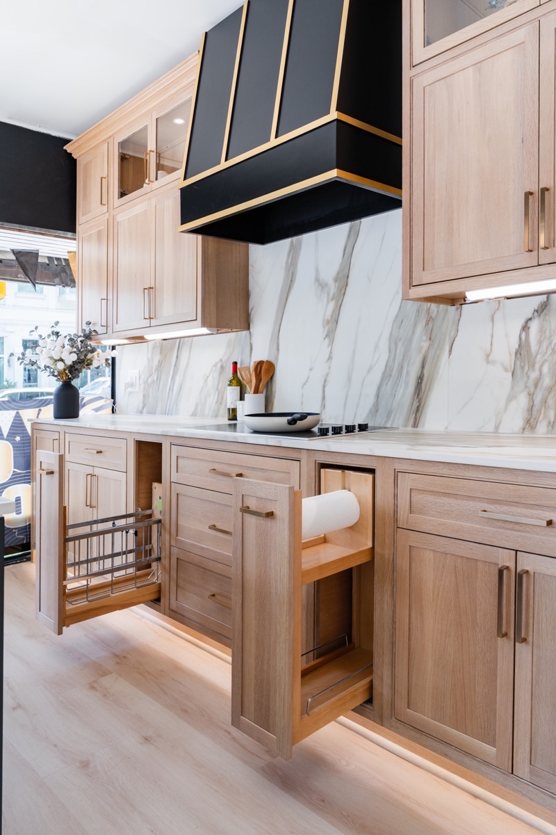 Kitchen display at the Bethesda Cabinets showroom with wood cabinets, a marble backsplash, and an open pull-out drawer.