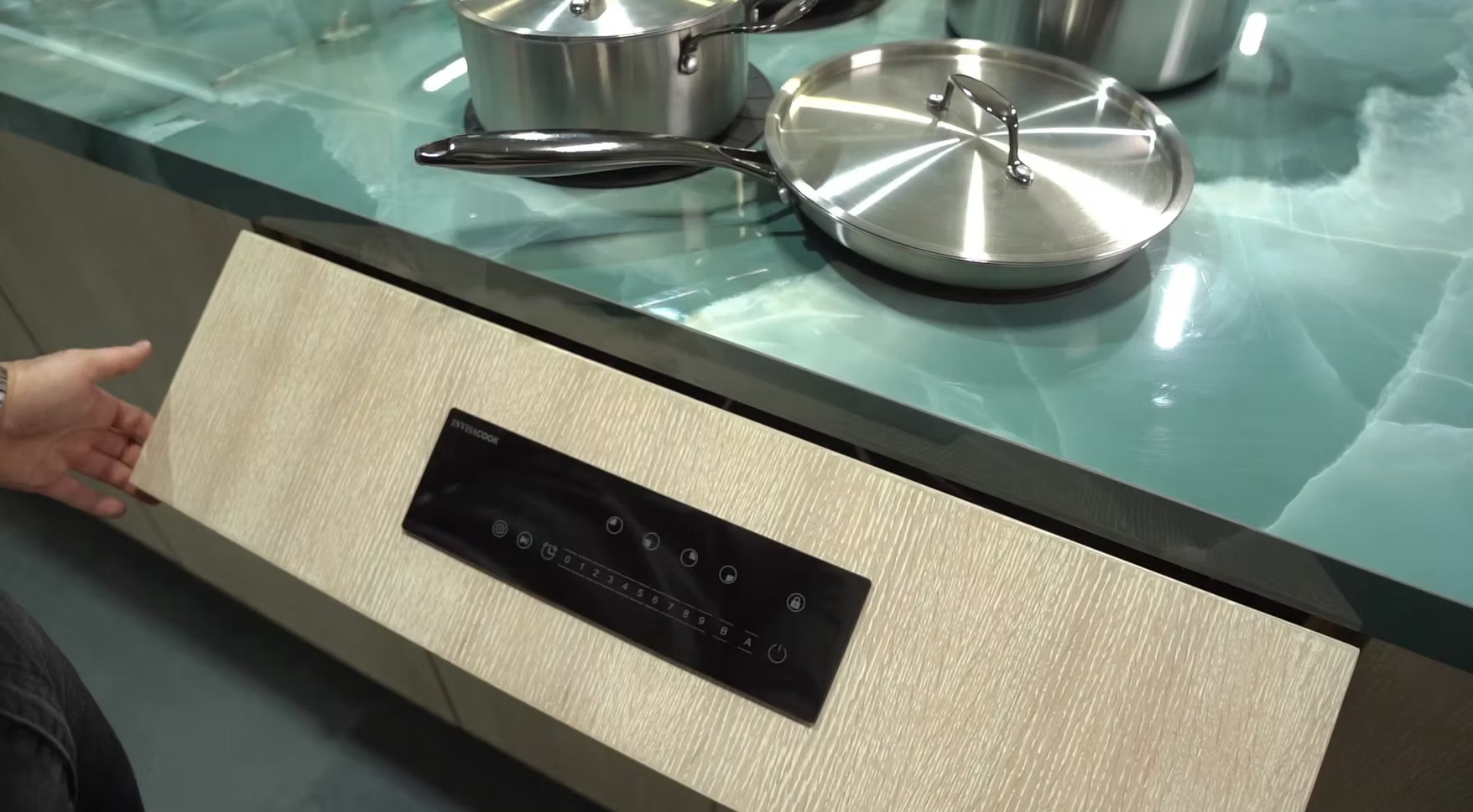 Invisacook unit built in under a glass countertop, with cookware sitting directly on the counter and the control panel set into the cabinet face.