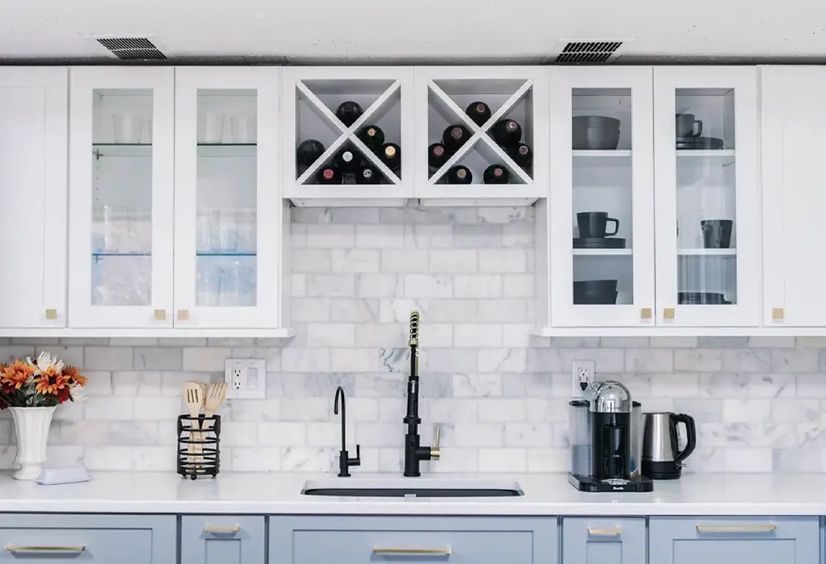 Kitchen display at the Bethesda Cabinets showroom with white cabinets, glass-front uppers, a wine rack, and a marble backsplash.