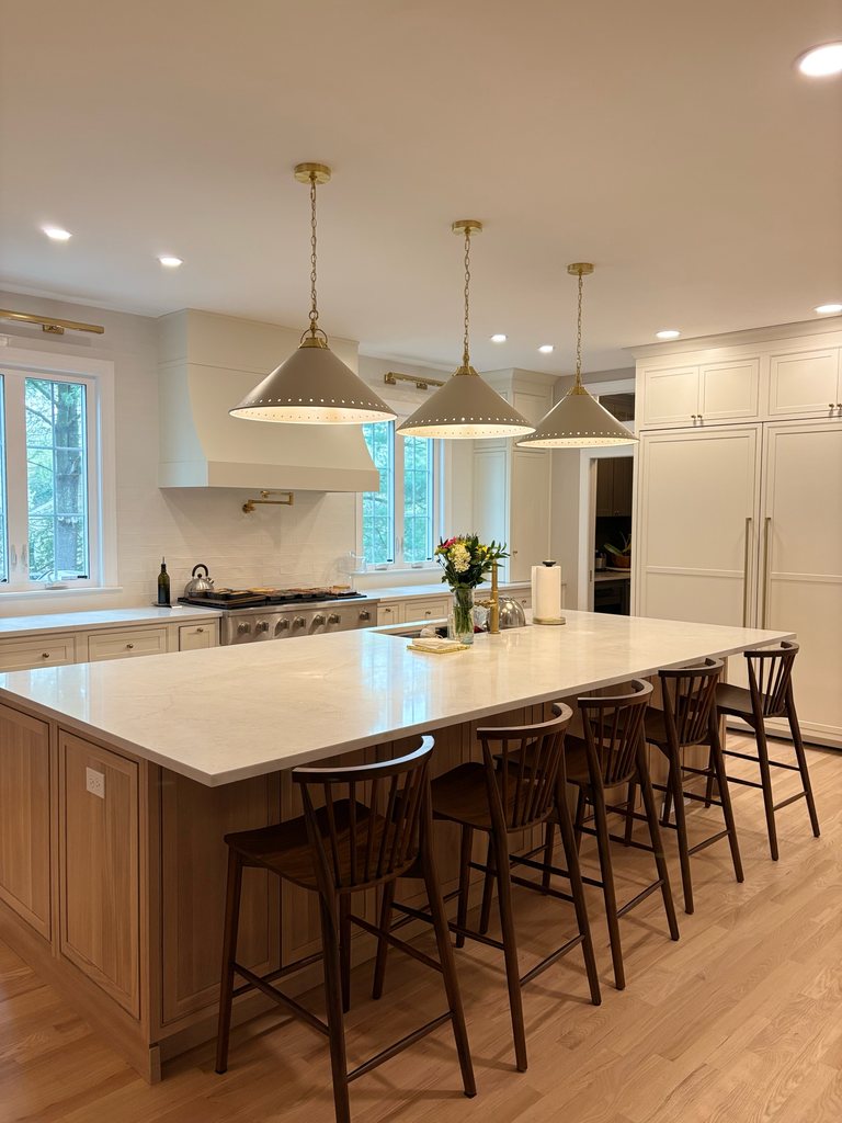 White oak kitchen island with an MSI quartz countertop and spindle-back stools, with Shiloh inset cabinetry in soft white and a range hood behind it, a Bethesda Cabinets project.