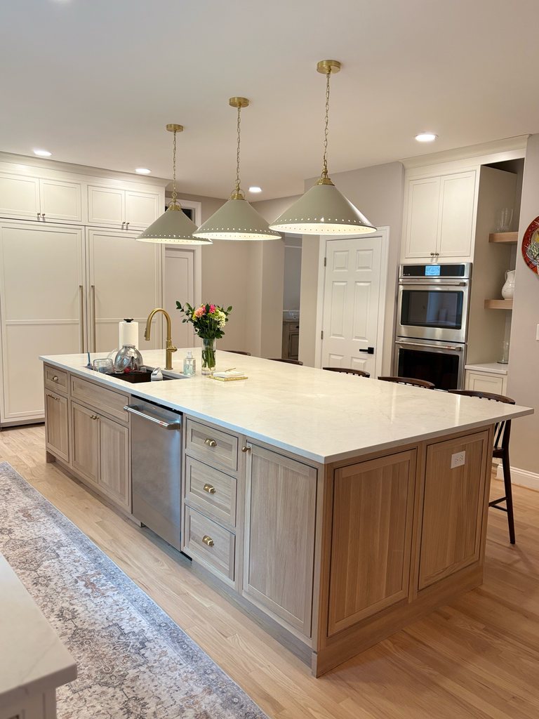 White oak island with an MSI quartz countertop facing Shiloh inset wall cabinetry in soft white with built-in wall ovens, a Bethesda Cabinets project.