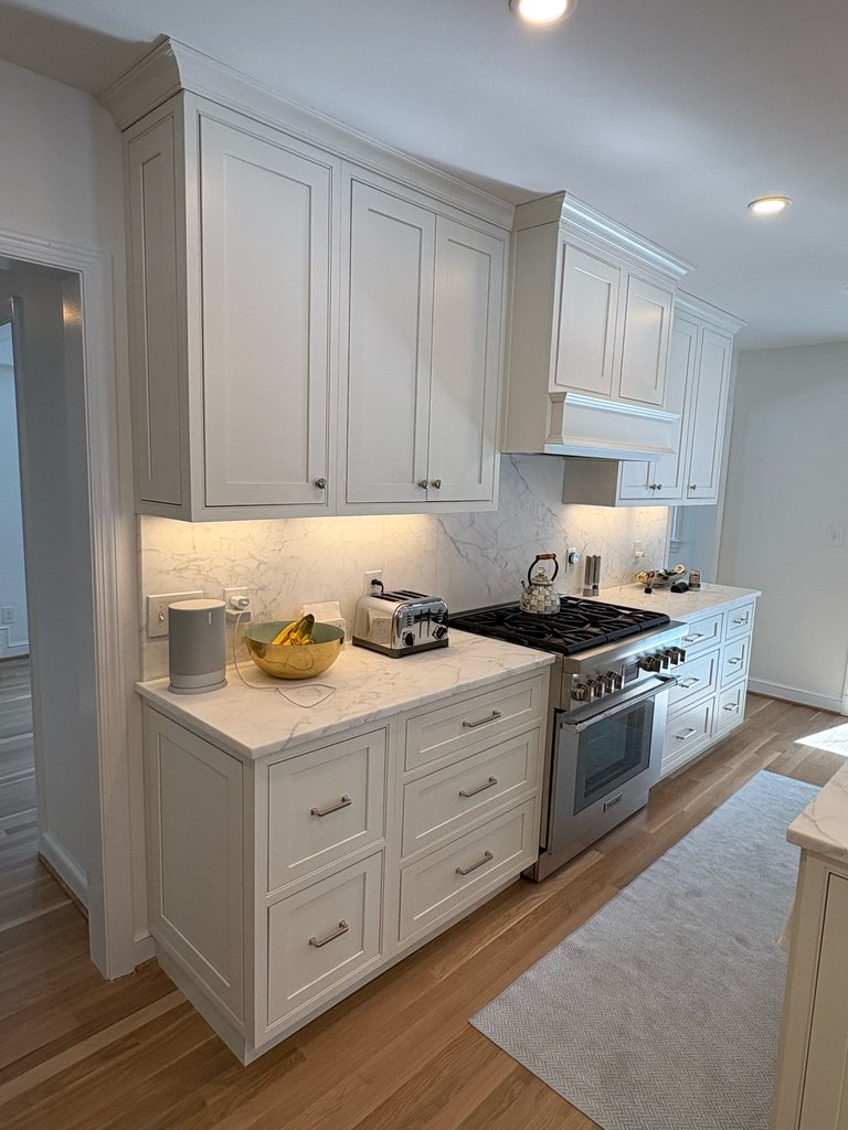 Shiloh beaded inset kitchen cabinetry in soft white with a stone backsplash, a stainless range and a white range hood, a Bethesda Cabinets project.