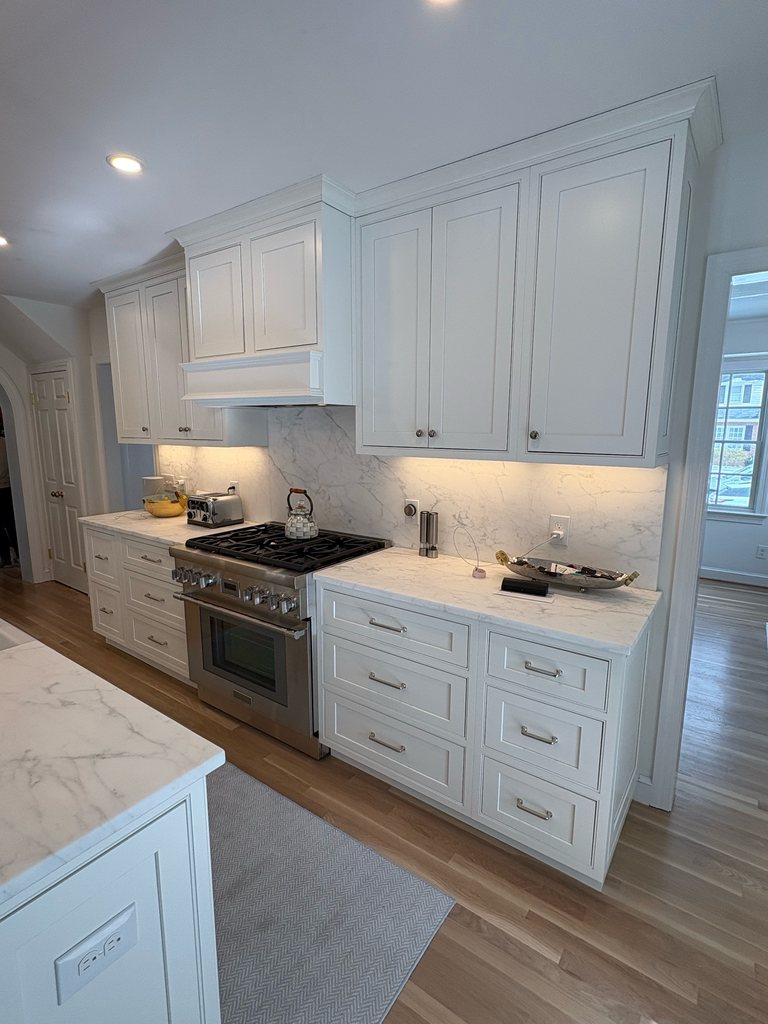 Shiloh beaded inset cabinetry in soft white with quartzite countertops and a stone backsplash around a stainless range, a Bethesda Cabinets project.