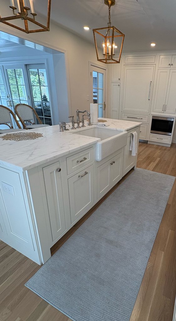 White kitchen island with a quartzite countertop, a farmhouse sink and a bridge faucet under lantern pendants, with Shiloh beaded inset cabinetry in soft white, a Bethesda Cabinets project.